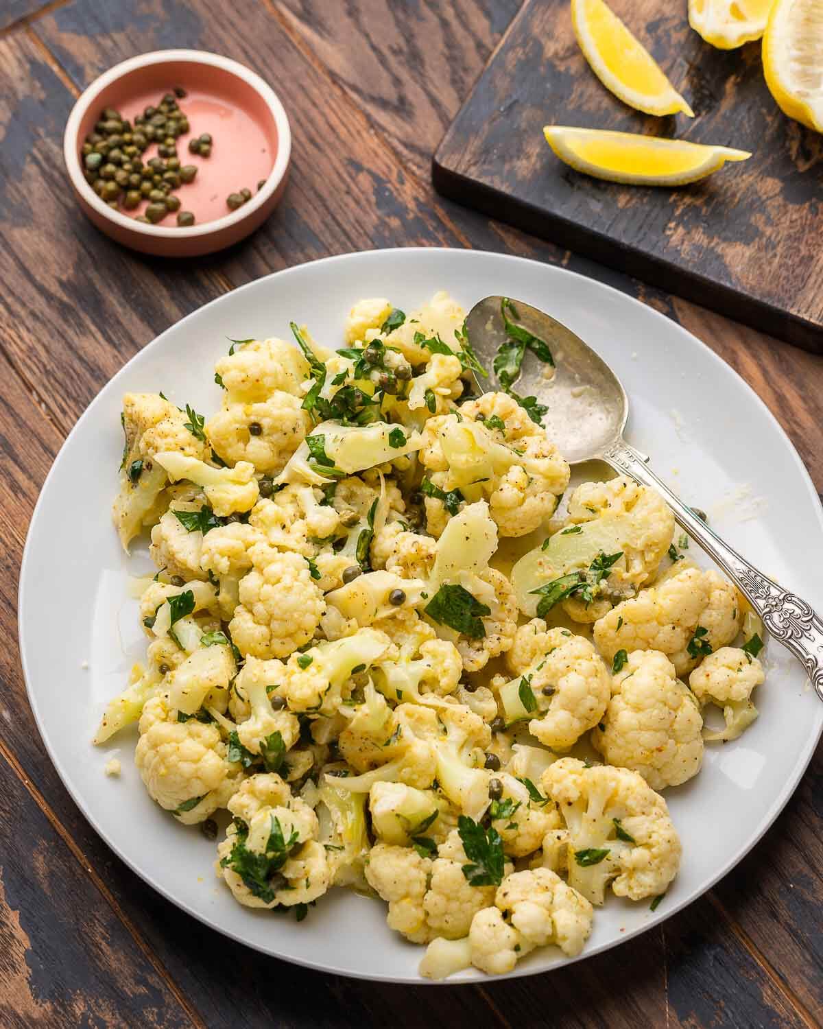 Cauliflower salad in white platter with lemons and capers on the side.