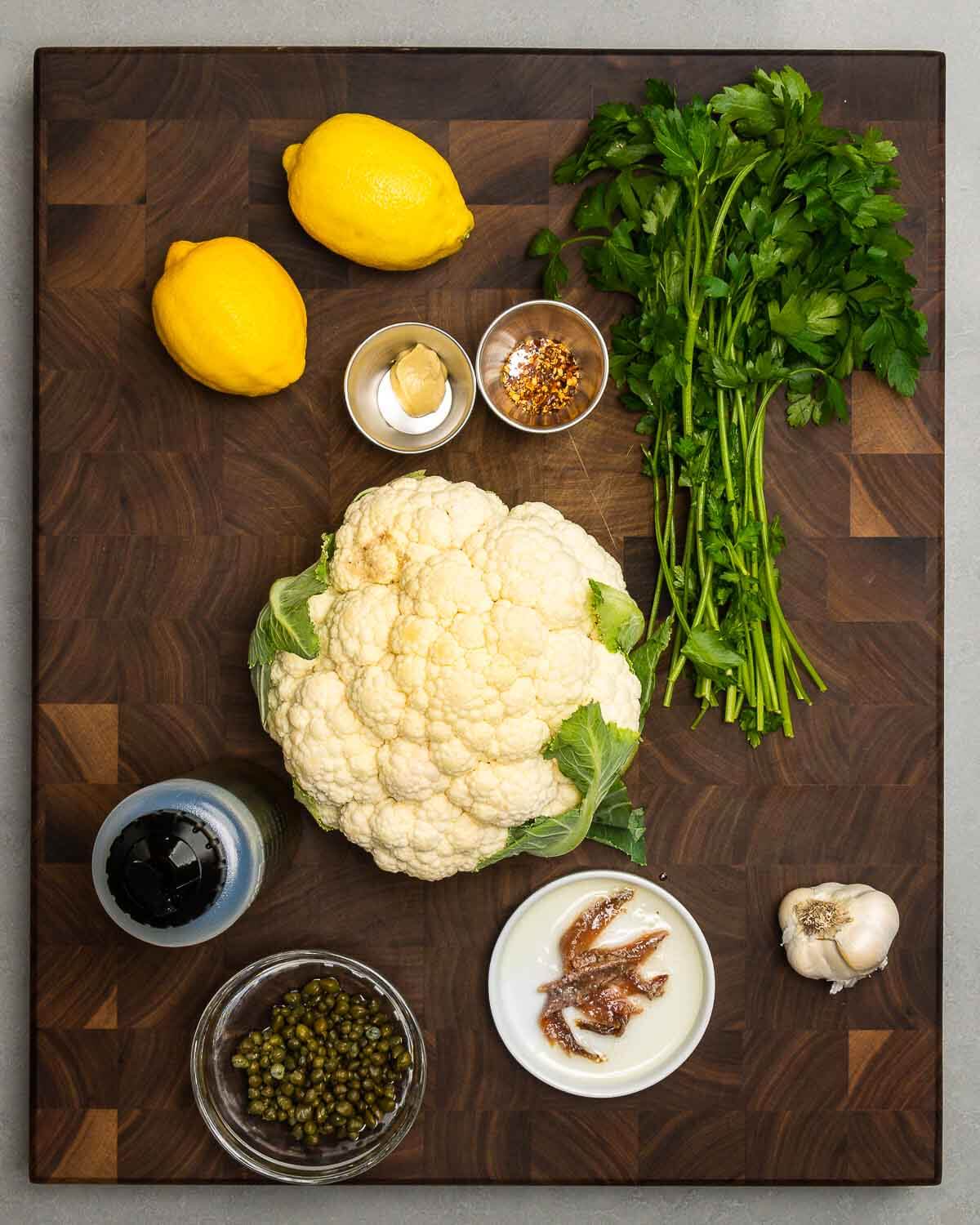 Ingredients shown: lemons, Dijon mustard, hot red pepper flakes, parsley, caulifower, olive oil, capers, anchovies, and garlic.