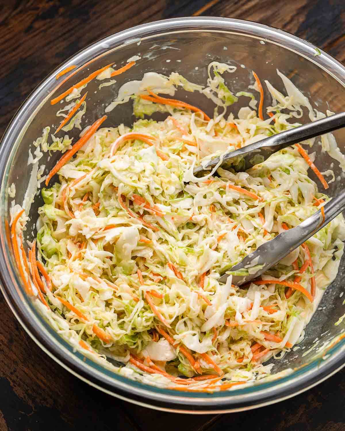 Large bowl with deli coleslaw and tongs.