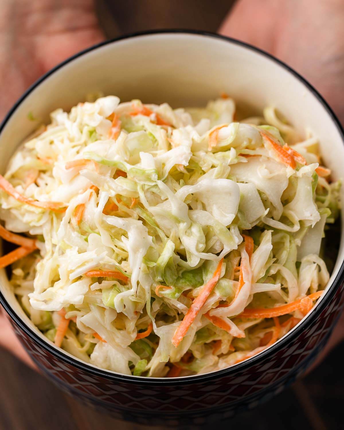 Hands holding small bowl of New York deli coleslaw.