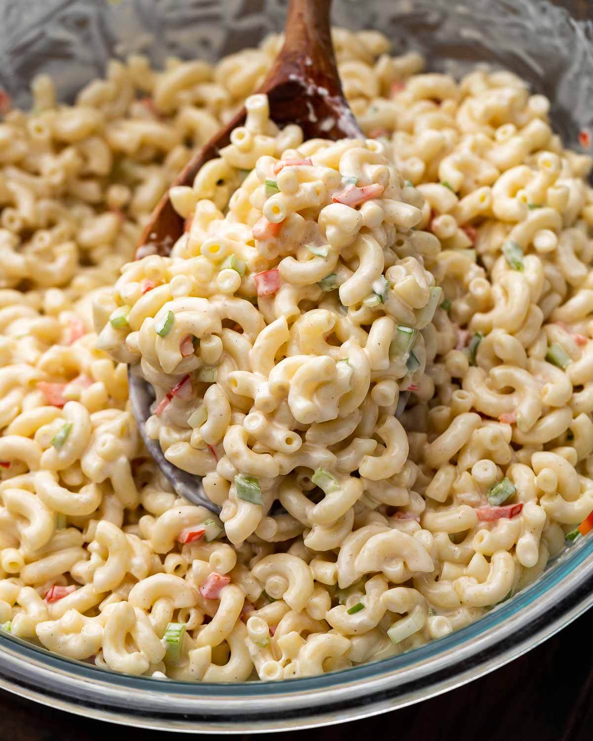 Deli macaroni salad in glass bowl with wooden spoon.