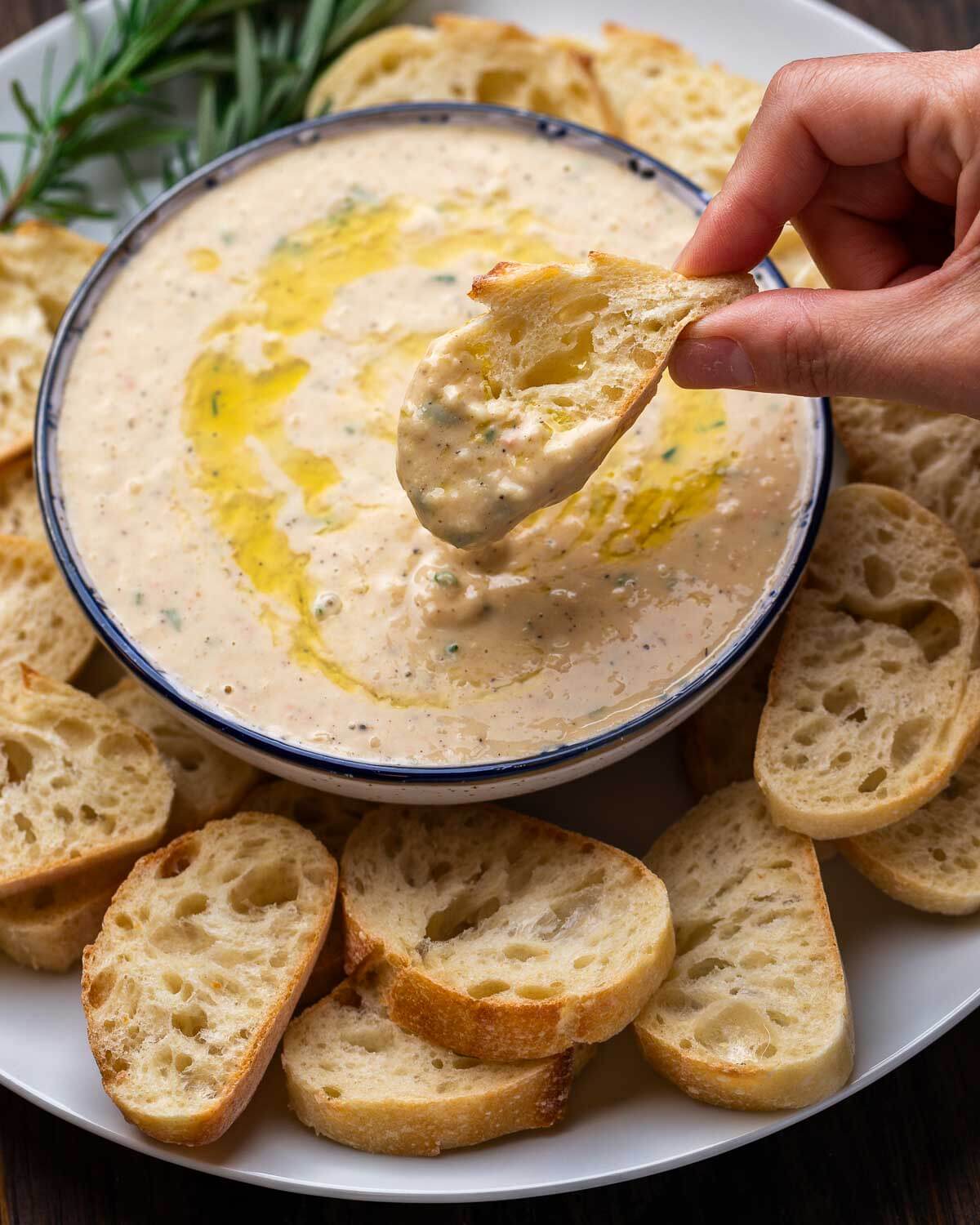Hand holding bread dipped into cannellini bean dip.