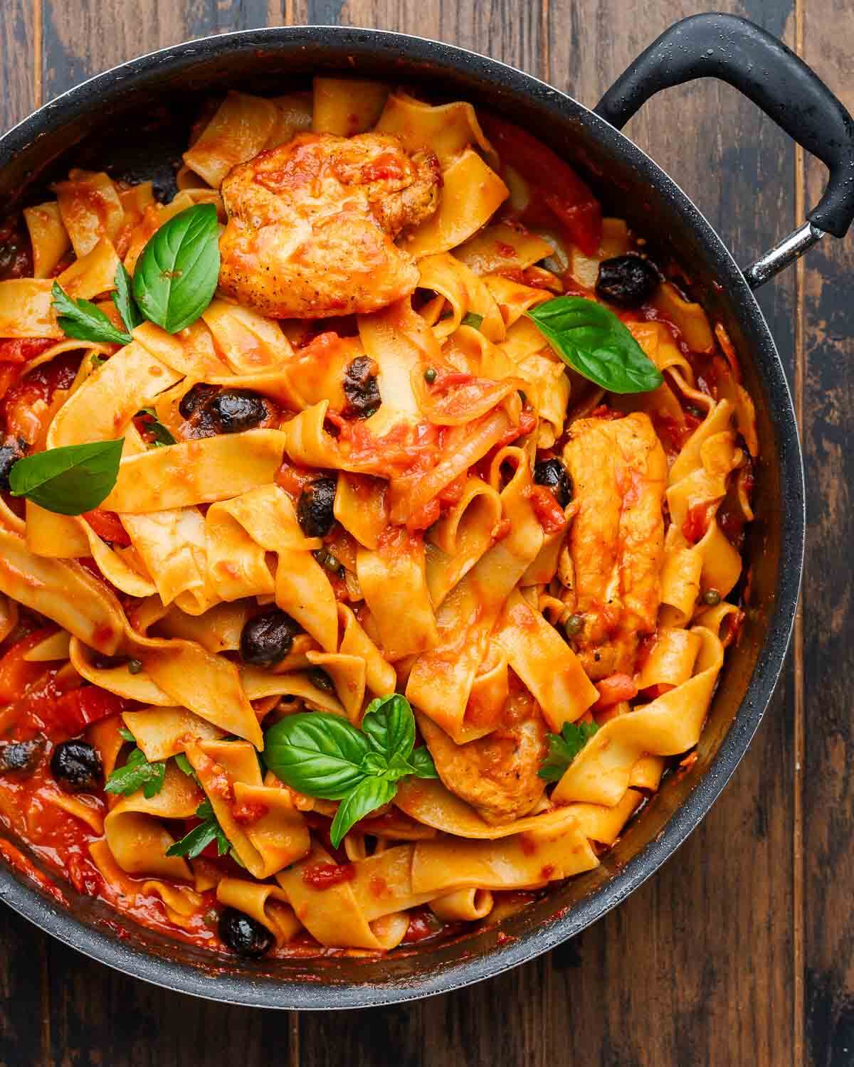 Closeup shot of large pan with chicken cacciatore pasta and basil garnish.