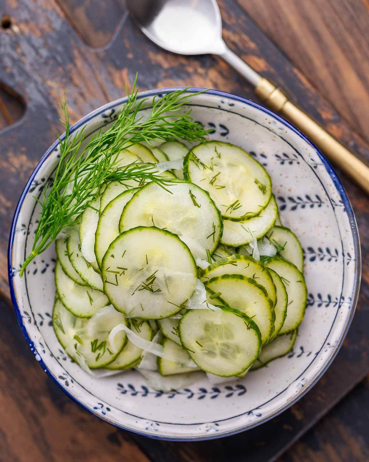 Closeup shot of cucumber salad in blue and white bowl with dill garnish.