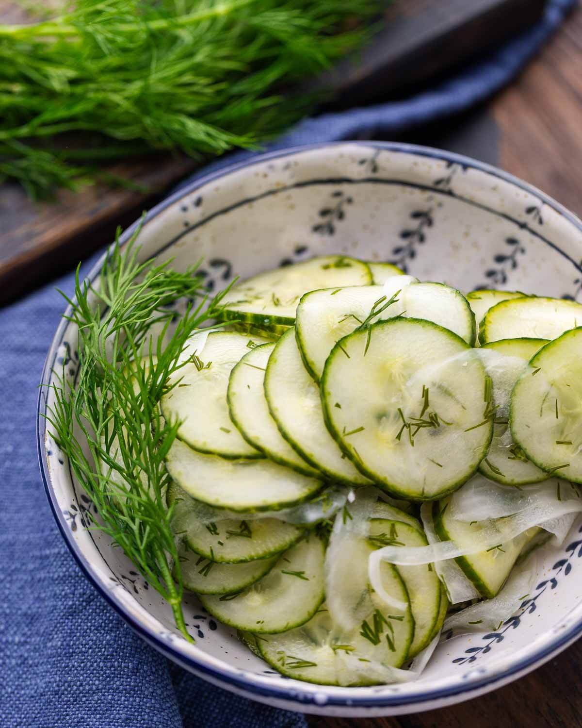 Closeup shot of cucumber salad in blue and white bowl with blue napkin in background.