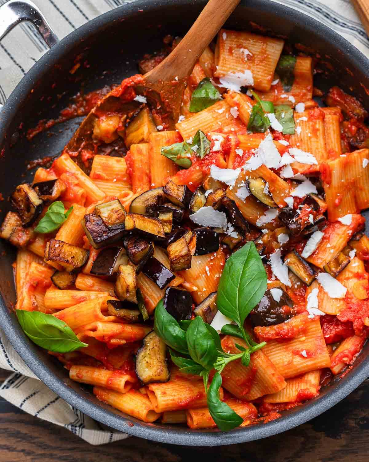 Overhead shot of pasta alla Norma in pan with shredded ricotta salata and basil.