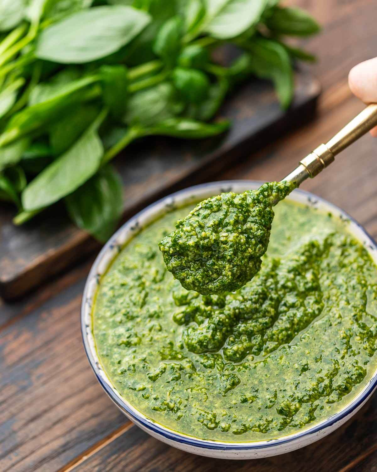 Hands holding spoonful of pesto alla Genovese above white and blue bowl.