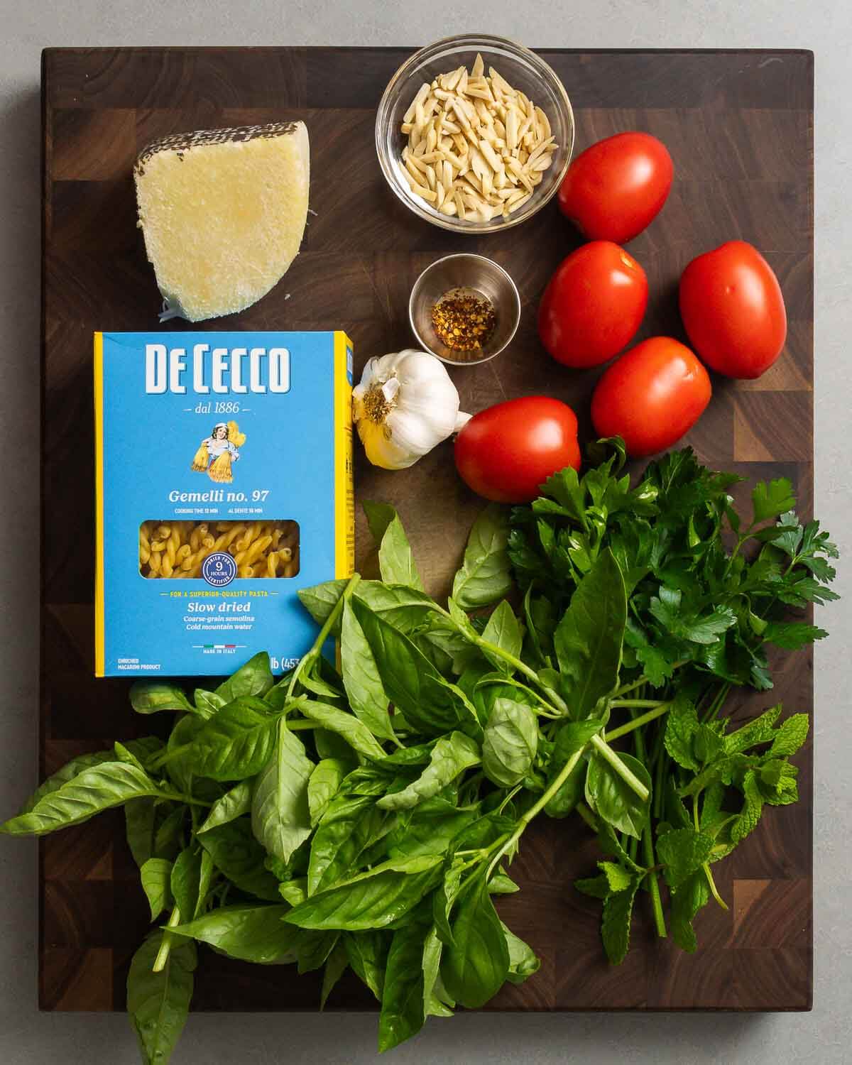 Ingredients shown: Pecorino Romano, almonds, hot red pepper flakes, plum tomatoes, pasta, garlic, basil, parsley, and mint.