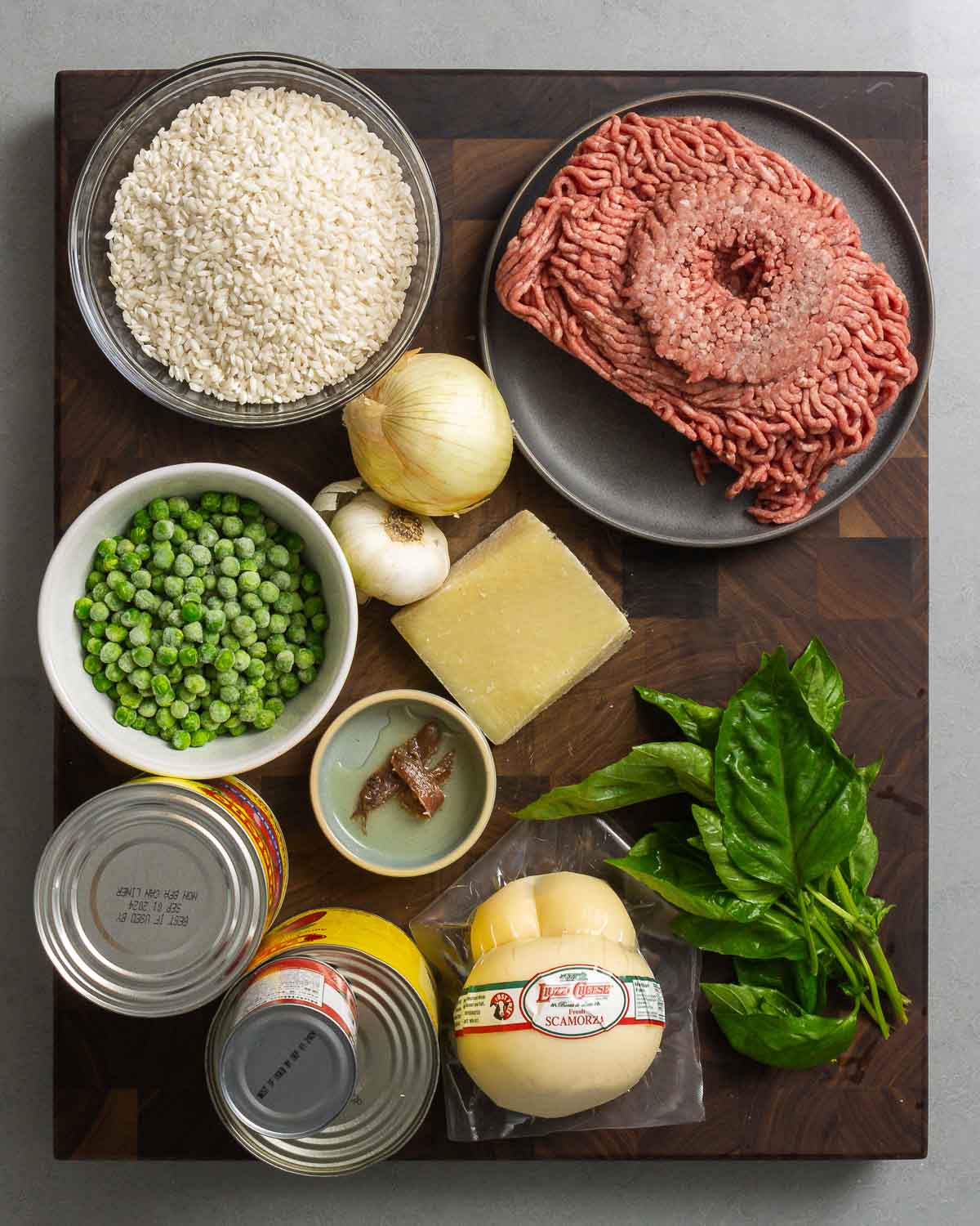 Ingredients shown: arborio rice, ground chuck, onion, garlic, peas, pecorino, scamorza, anchovy, tomatoes, and basil.