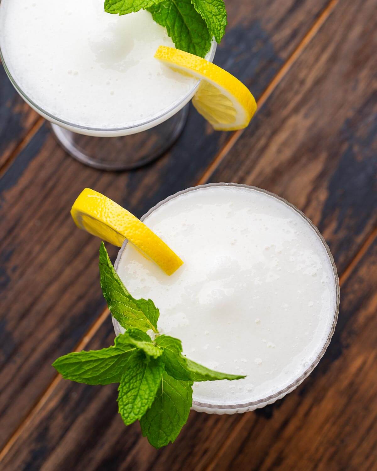 Overhead shot of two glasses with sgroppino cocktail garnished with lemon wedges and mint on top of a wood table.