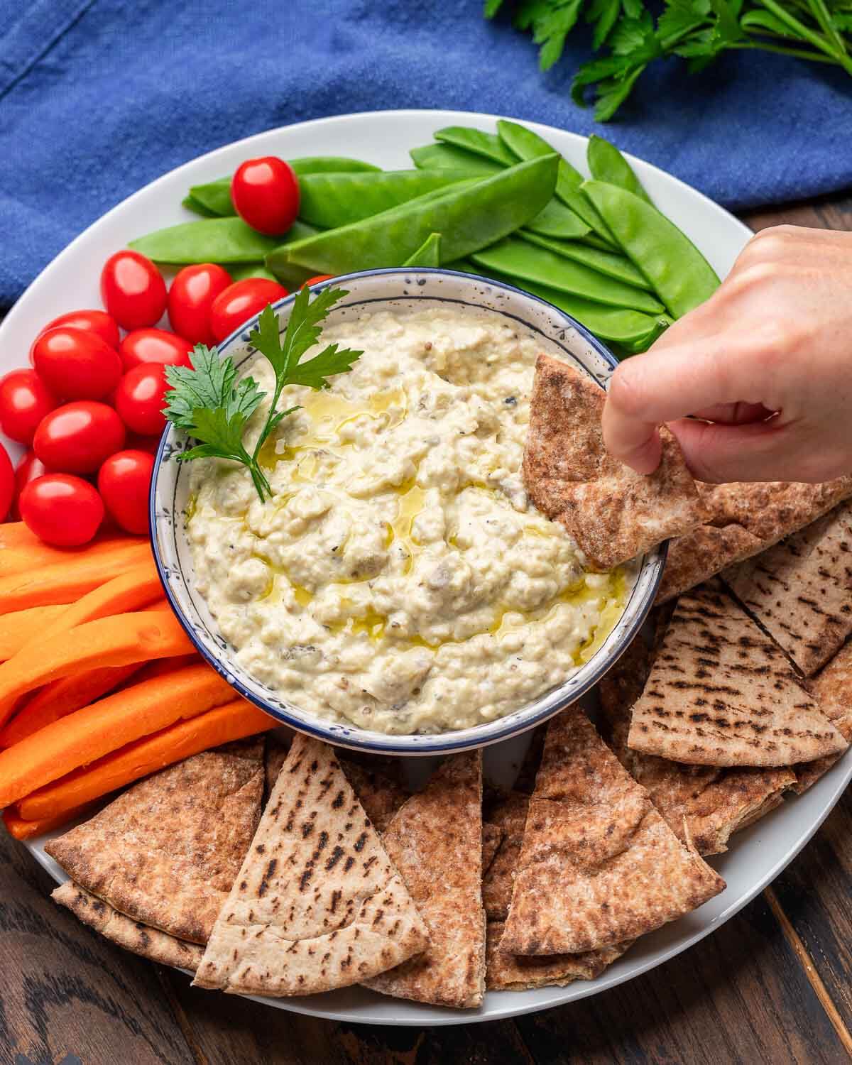 Overhead shot of baba ganoush platter with hands dipping pita into bowl.