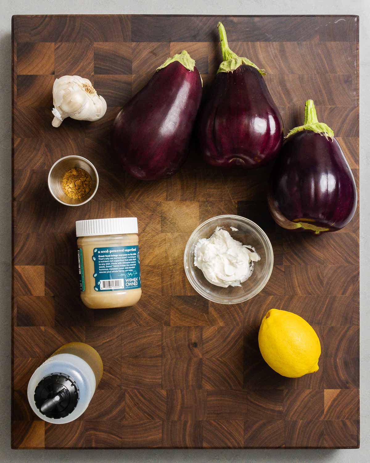 Ingredients shown: garlic, eggplants, cumin, tahini, Greek yogurt, extra virgin olive oil, and a lemon.
