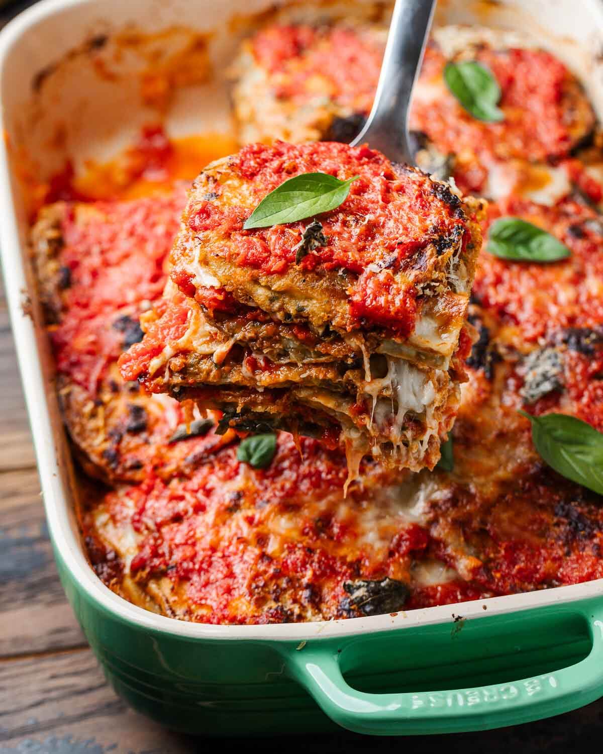 Spatula pulling out piece of eggplant parmesan from baking dish.