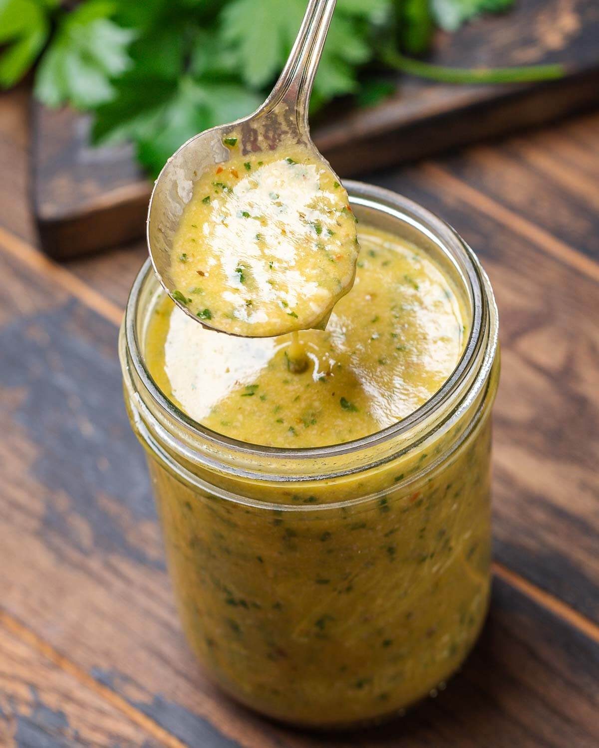 Spoon drizzling Italian vinaigrette over mason jar.