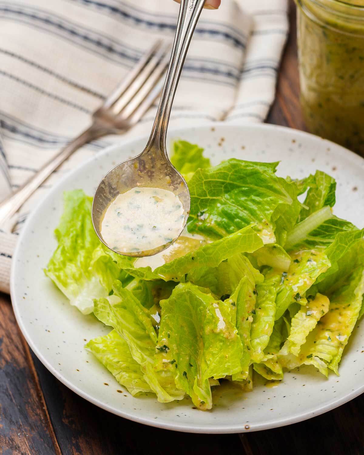 Spoon drizzling Italian vinaigrette onto a plate of salad.