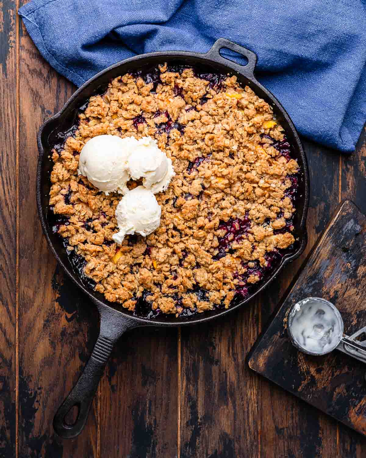 Overhead shot of peach blueberry crisp in cast iron pan with vanilla ice cream on top.