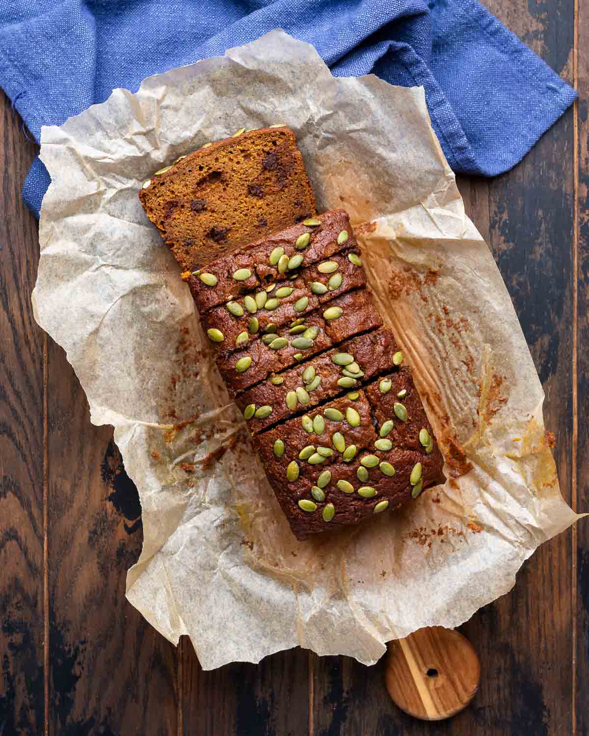 Overhead shot of sliced pumpkin bread topped with pumpkin seeds on top of parchment paper.