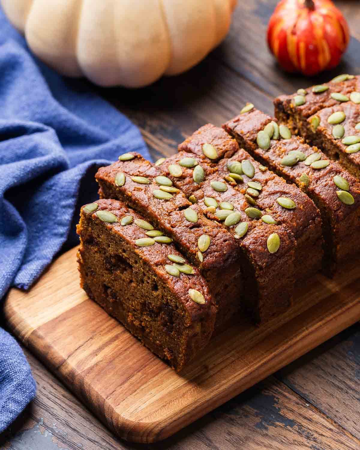 Sliced pumpkin bread on a wood board with white and orange pumpkins in the background.