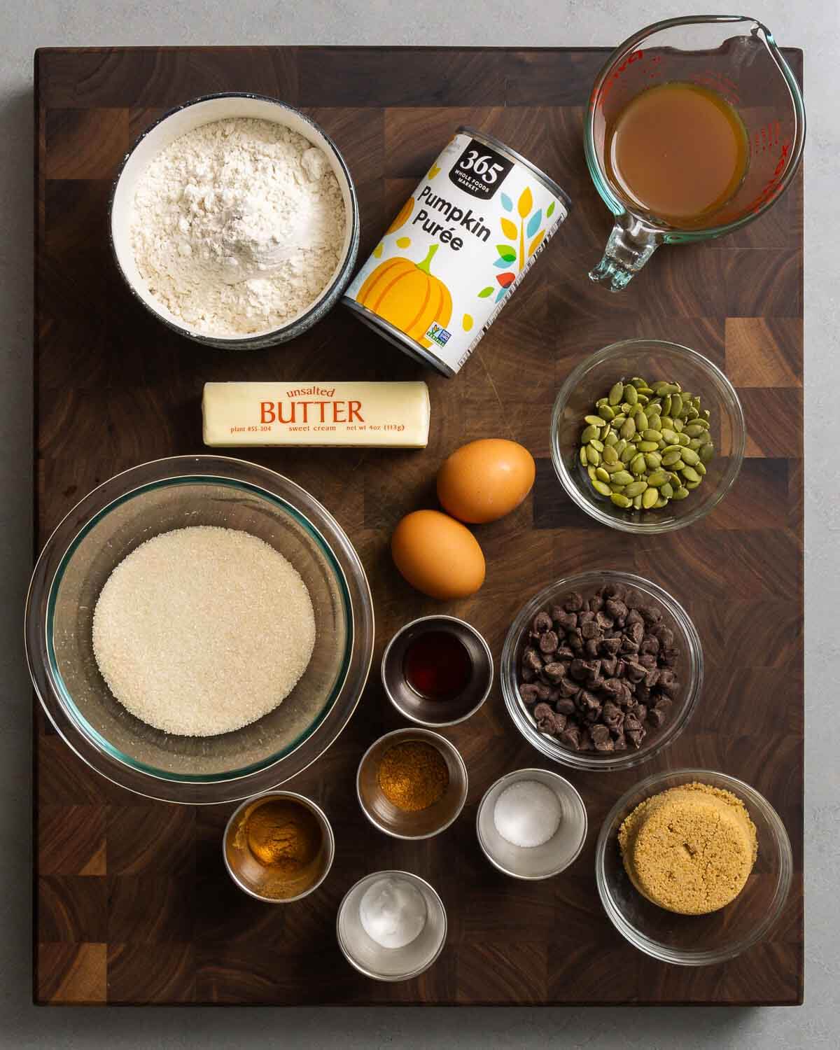 Ingredients shown: flour, pumpkin puree, apple cider, butter, eggs, pumpkin seeds, sugar, vanilla, cinnamon, baking soda, salt, brown sugar, and chocolate chips.
