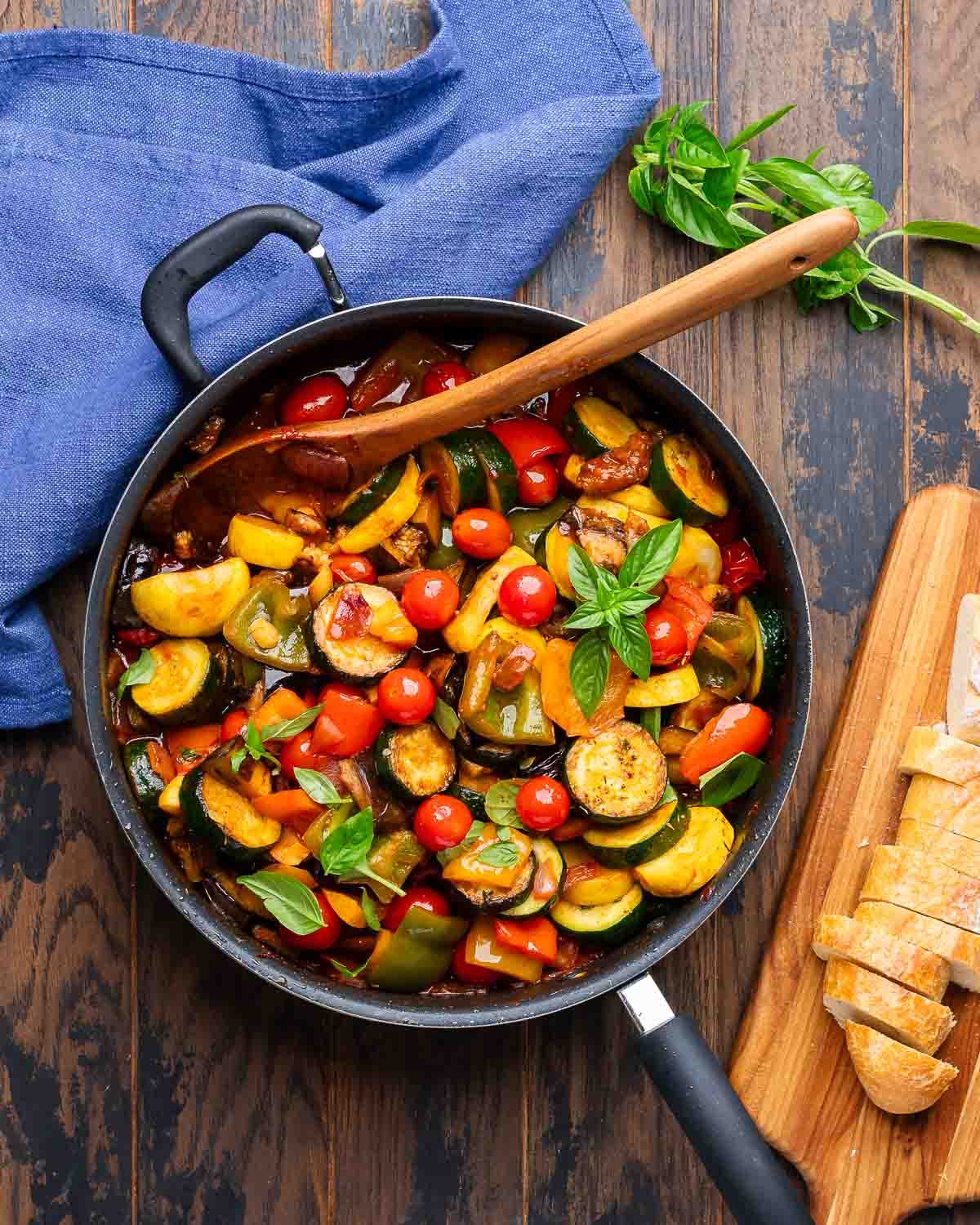 Overhead shot of ratatouille in black pan with basil and baguette on the side.