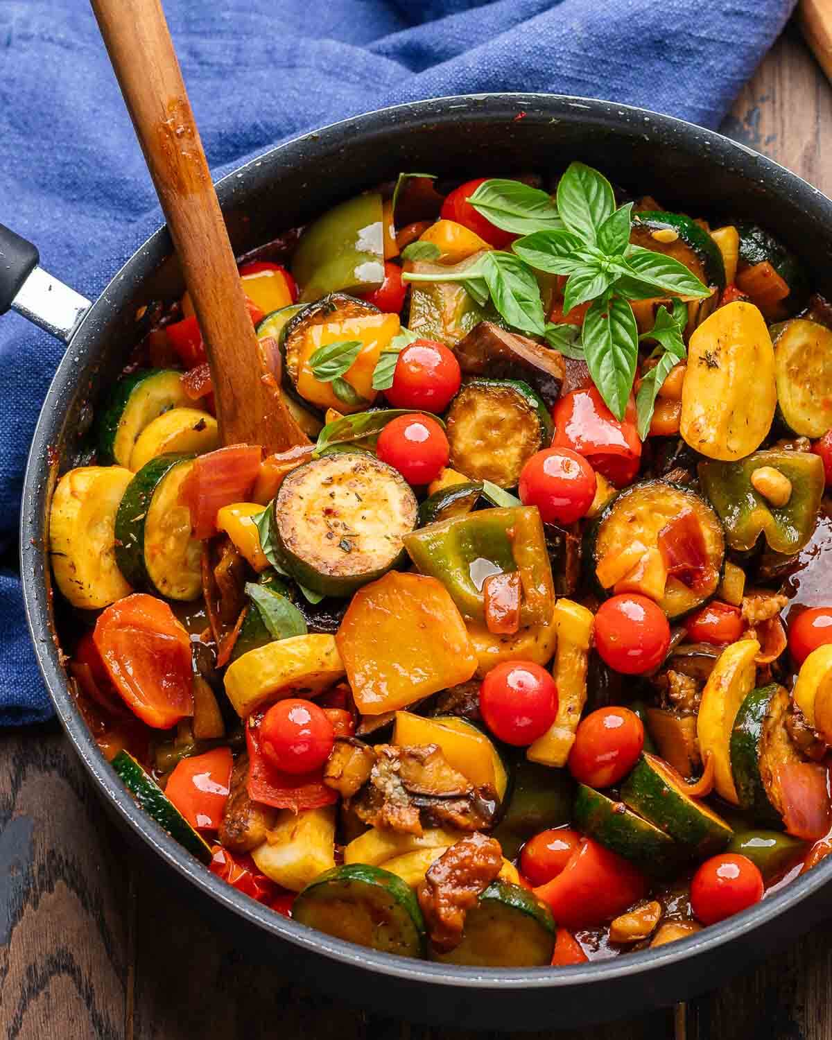 Ratatouille in black pan with wooden spoon and blue napkin.