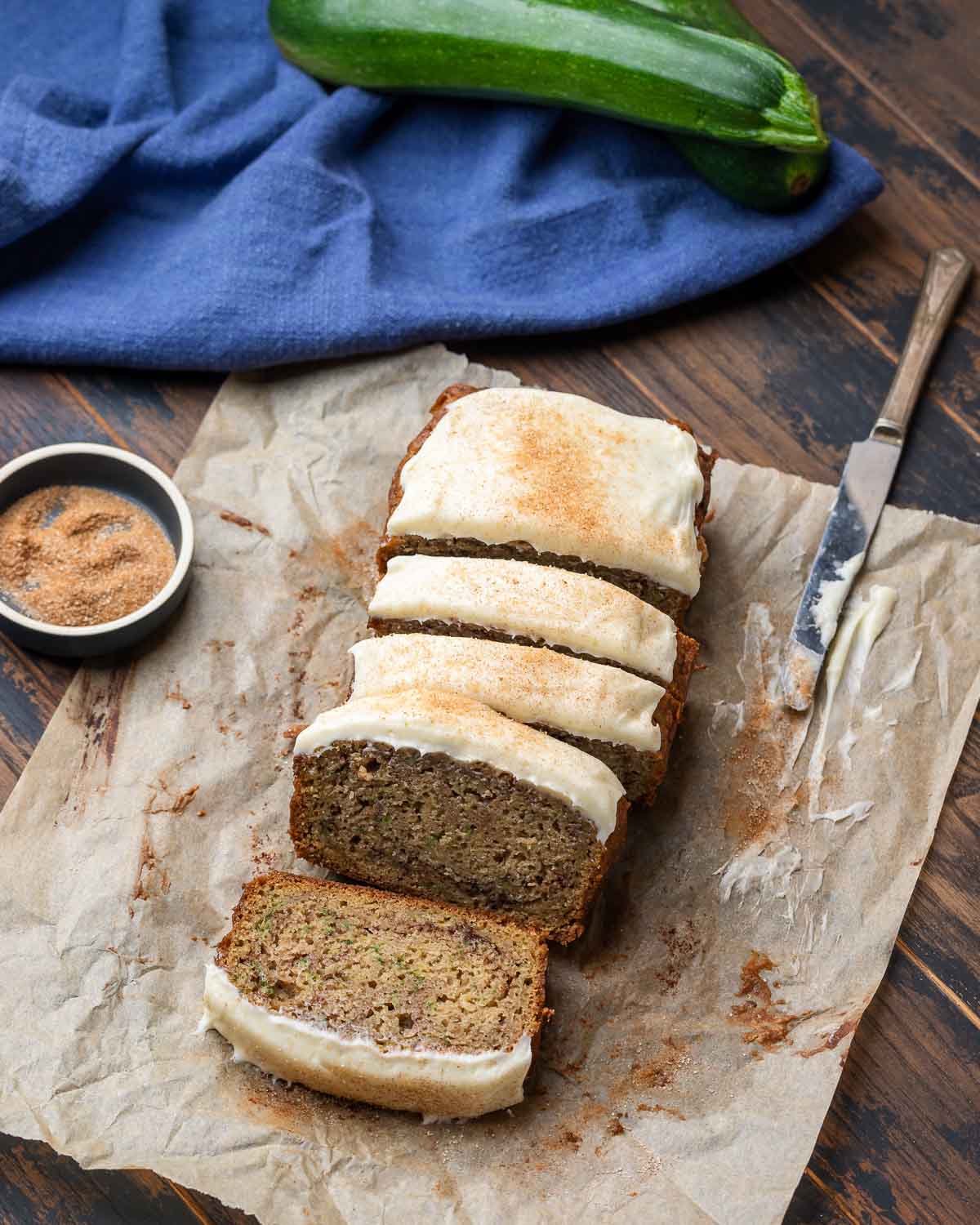 Overhead shot of cut zucchini bread with cream cheese frosting on top of parchment paper.