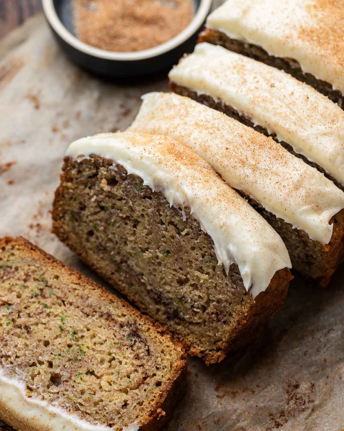 Closeup shot of 4 slices of zucchini bread with sprinkled cinnamon sugar and cream cheese frosting.