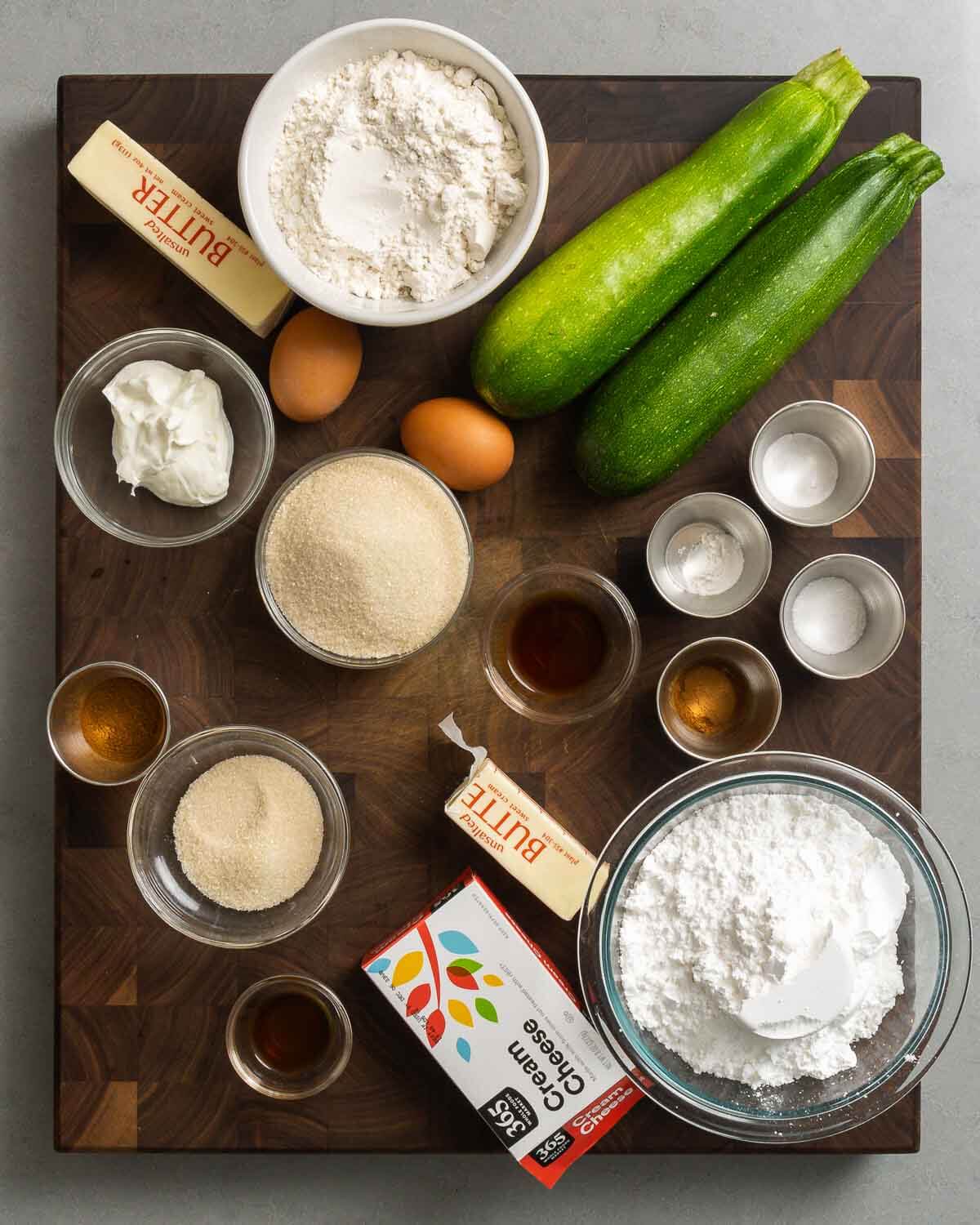 Ingredients shown: butter, flour, zucchini, eggs, Greek yogurt, sugar, baking soda, baking powder, salt, cinnamon, and vanilla.