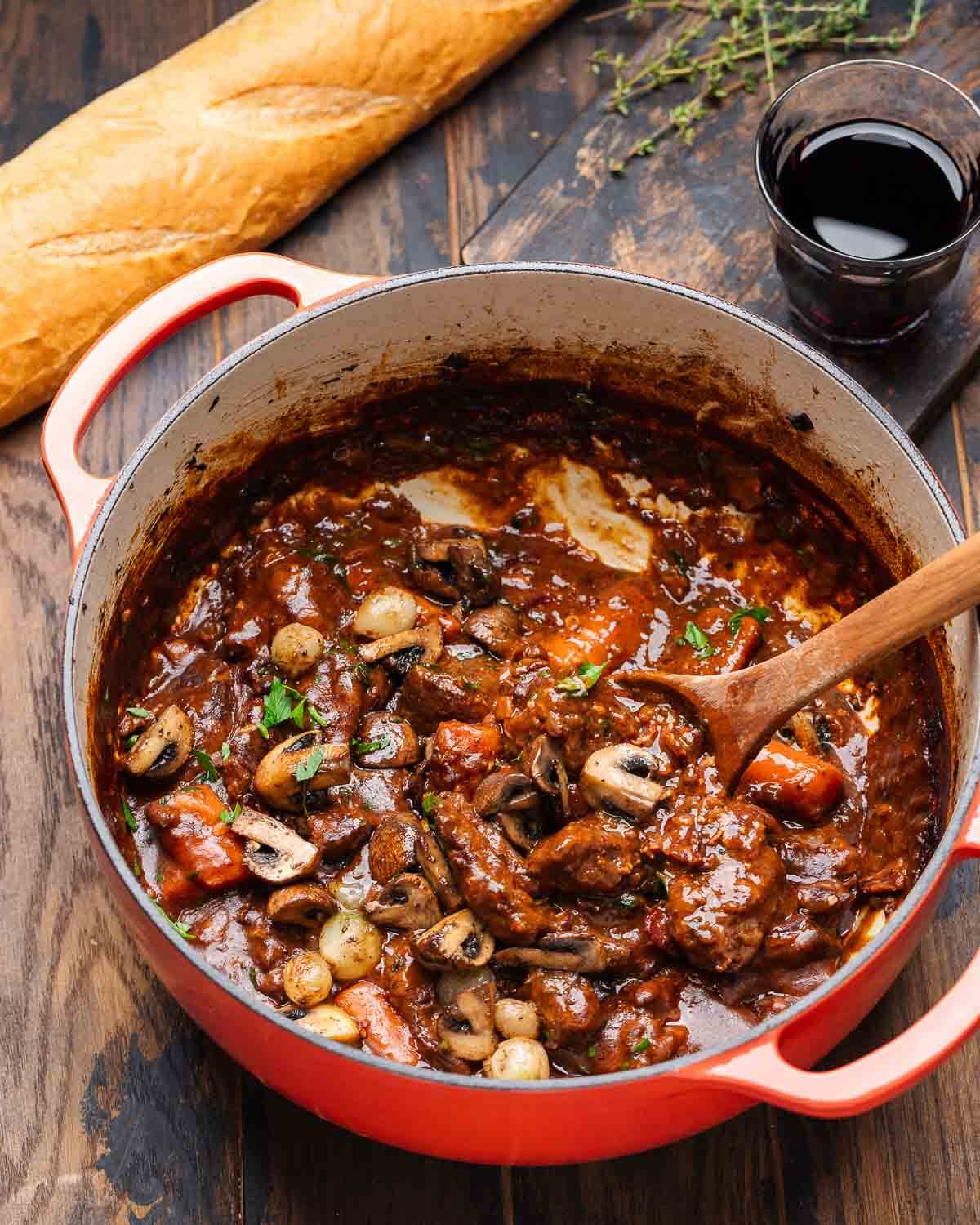Beef Bourguignon in Dutch oven with baguette and glass of red wine.