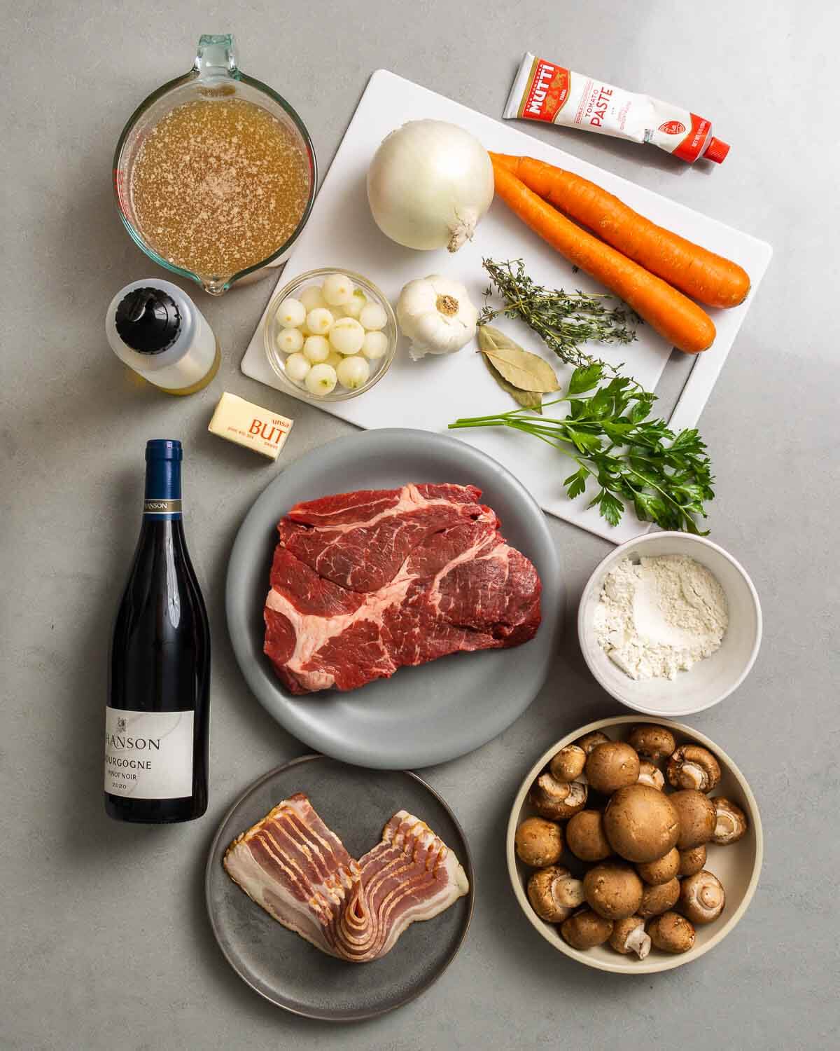 Ingredients shown: beef stock, olive oil, butter, pearl onions, garlic, onion, thyme, bay leaves, parsley, carrots, tomato paste, Burgundy wine, beef, bacon, flour, and mushrooms.