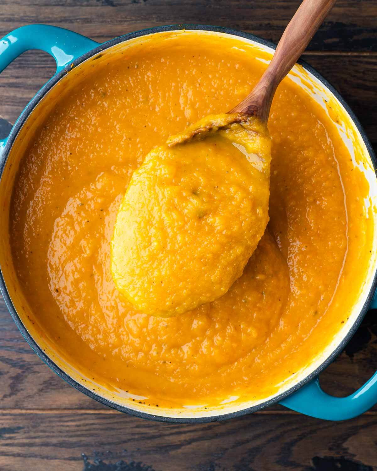 Large spoon scooping out butternut squash soup from Dutch oven pot.