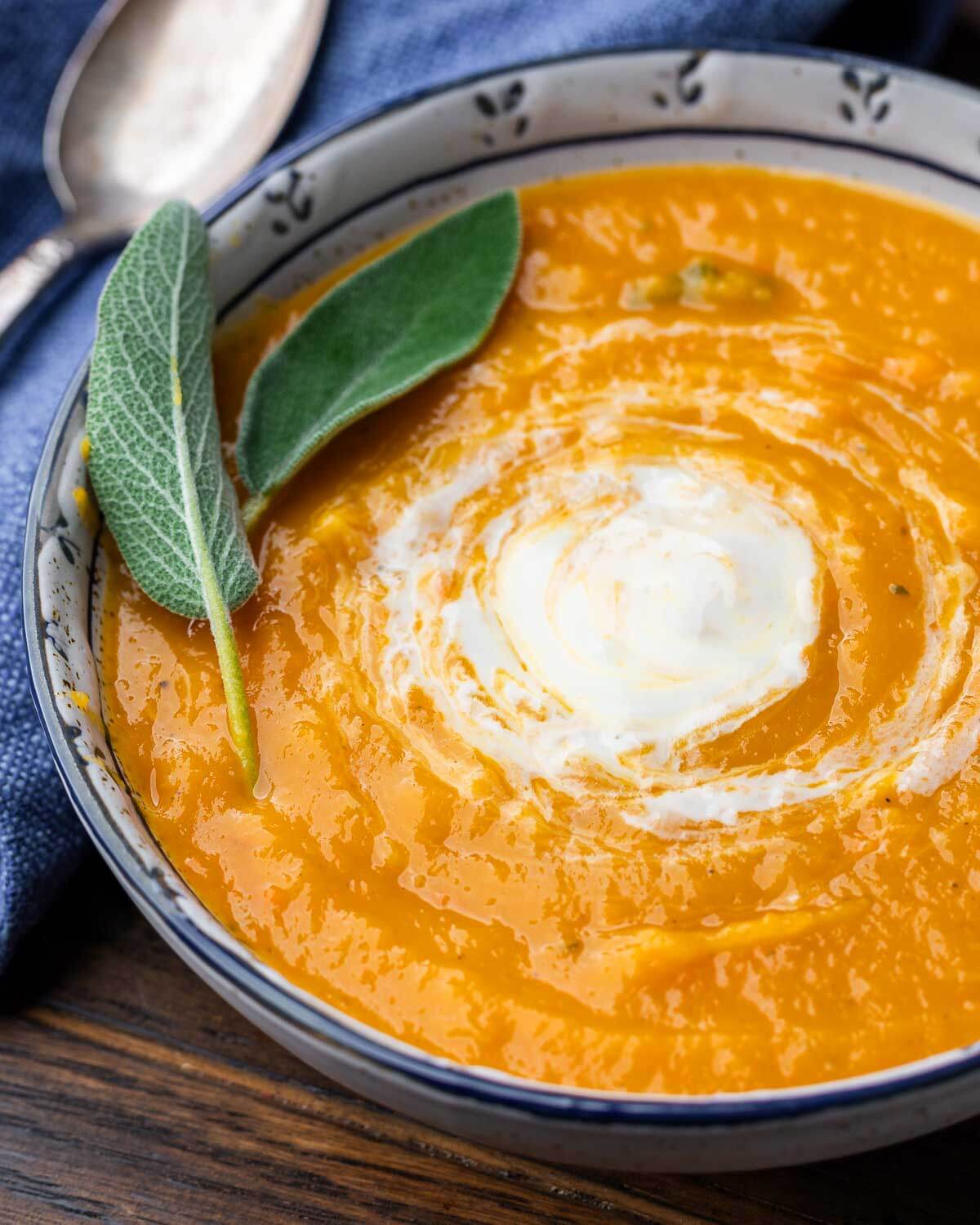 Roasted butternut squash soup in white and blue bowl with sage leave garnish.