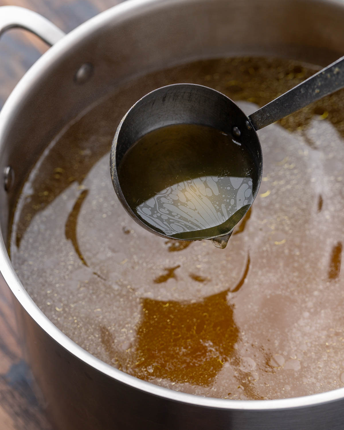 Ladle pouring chicken stock over stockpot.