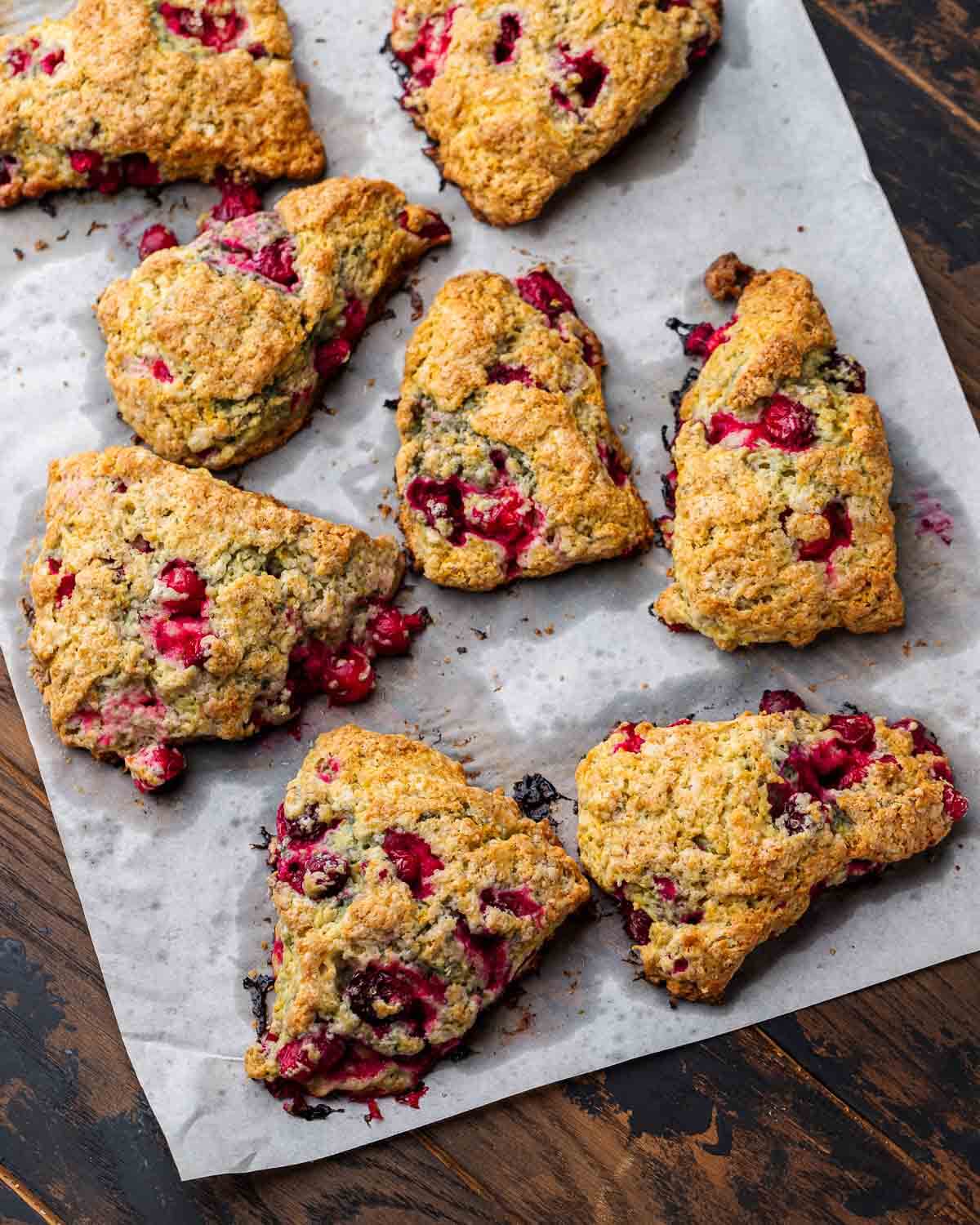 Eight cranberry orange scones on top of parchment paper on table.