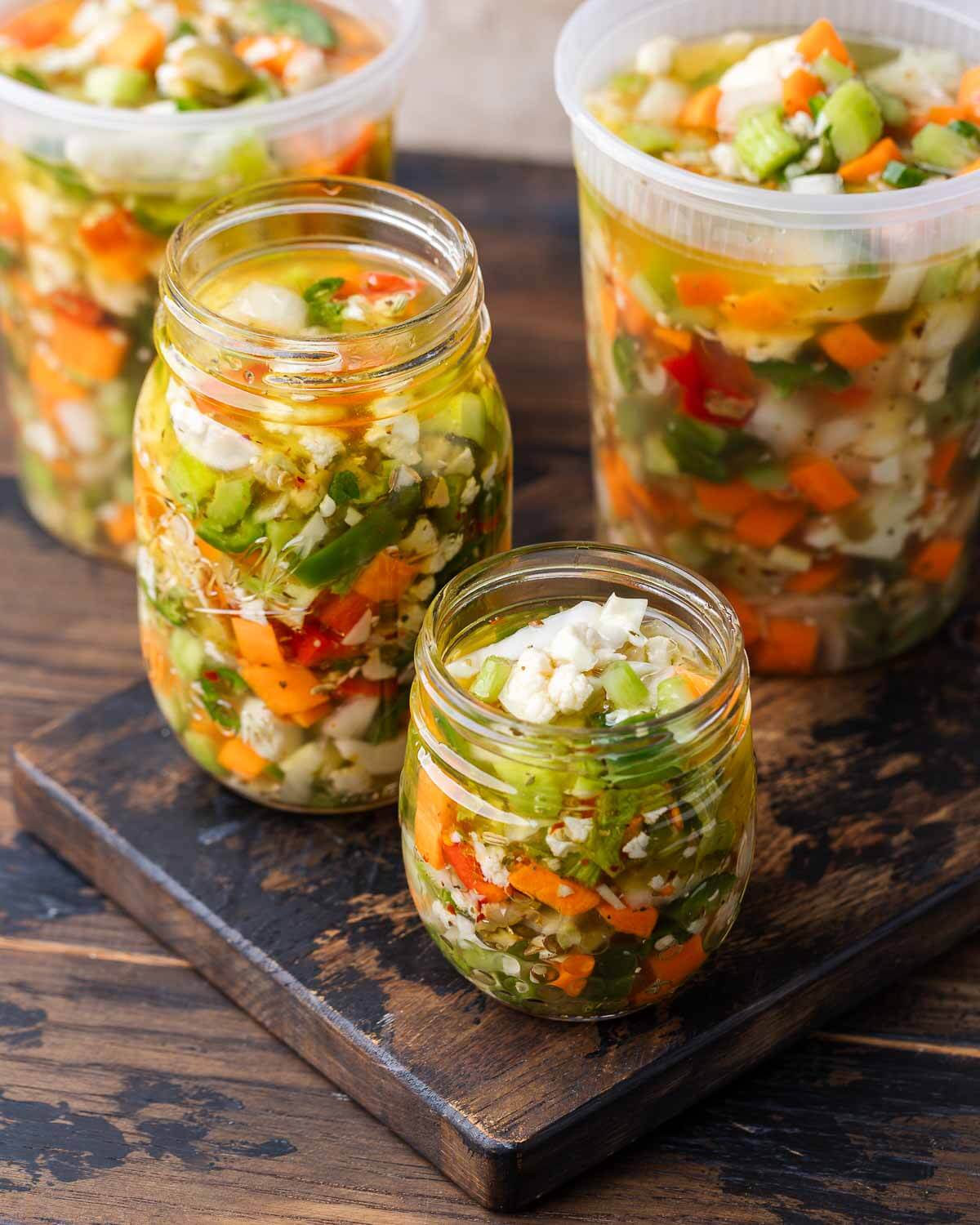 Quart containers and mason jars filled with giardiniera on wooden table.