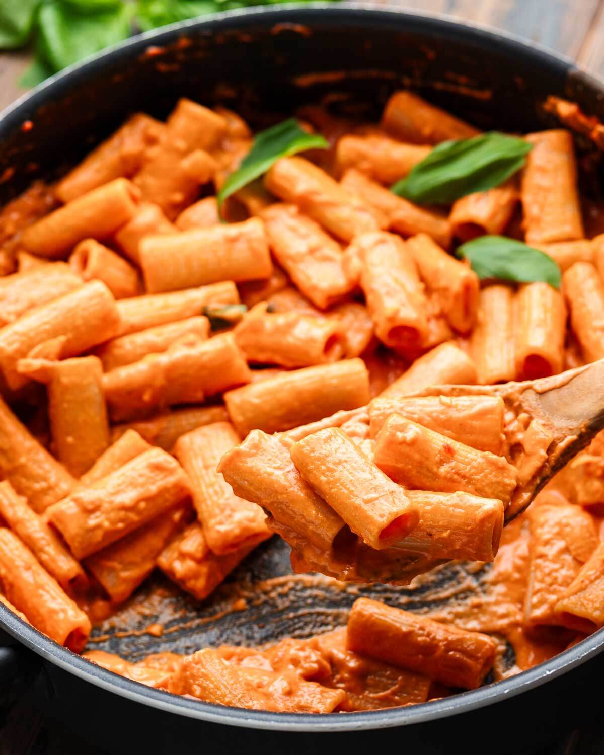 Large pan of rigatoni all vodka with wooden spoon scooping out pasta.