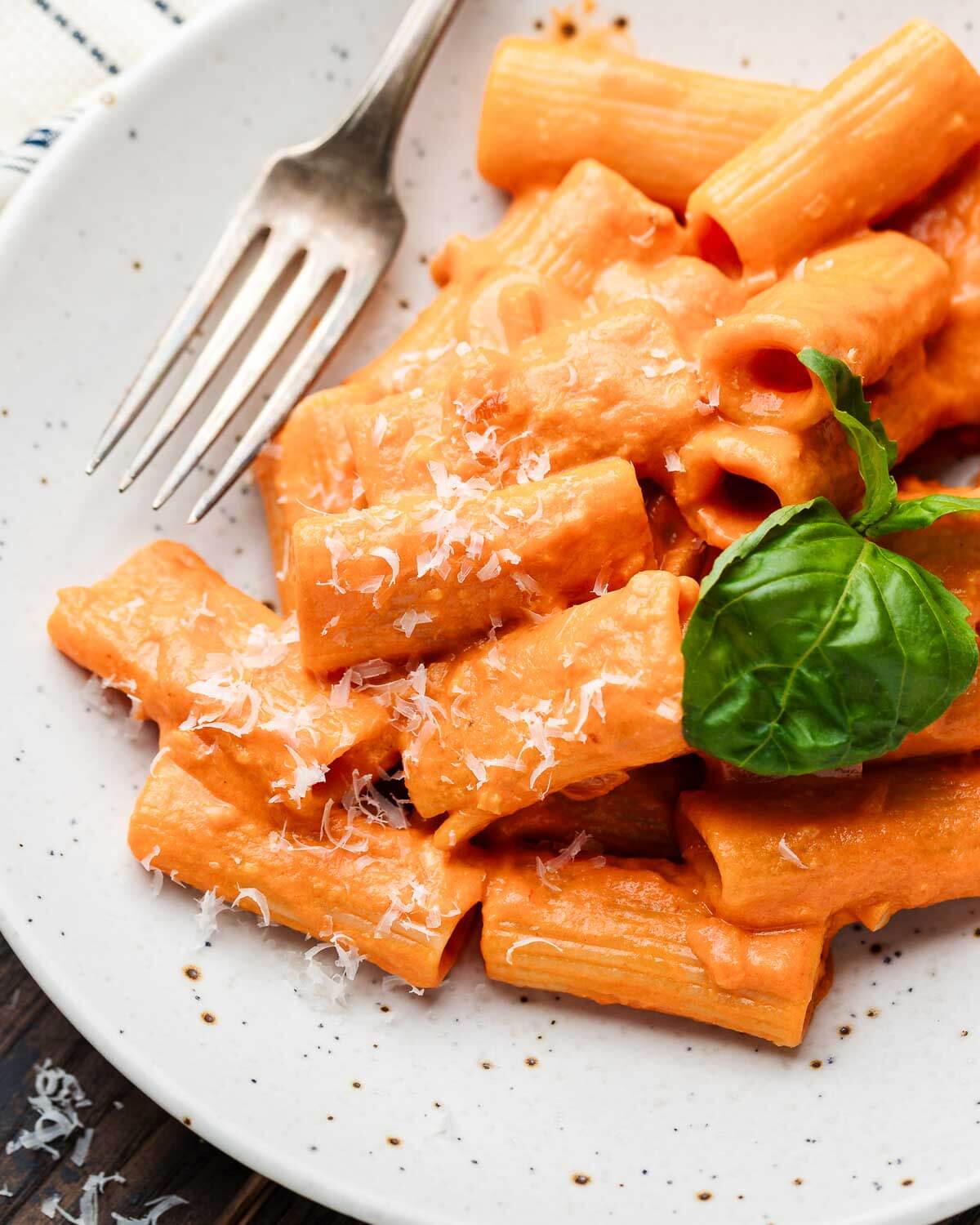 Rigatoni alla vodka in white plate with basil and grated cheese.