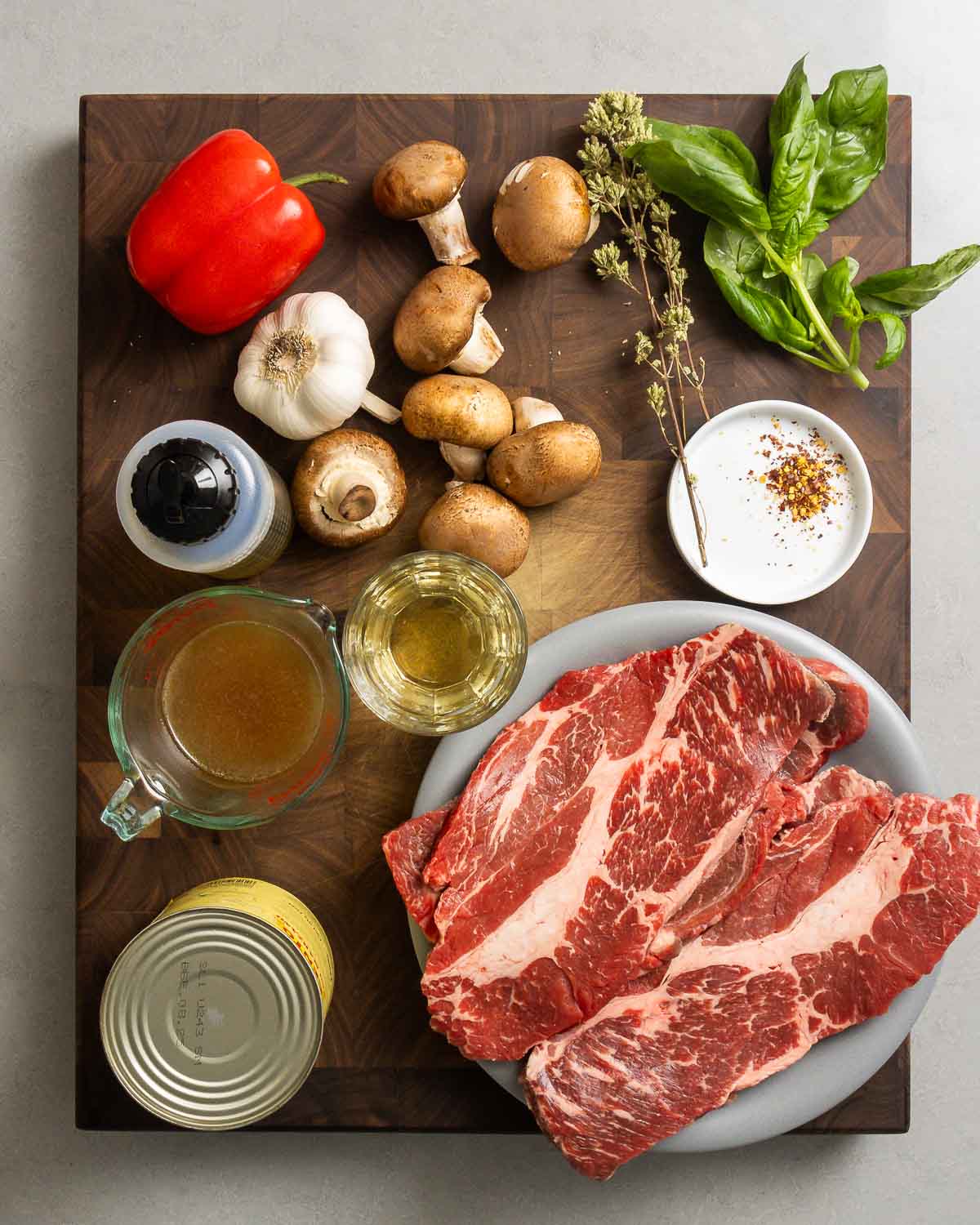 Ingredients shown: stuck cheaks, red bell pepper, mushrooms, oregano, basil, garlic, olive oil, beef stock, white wine, red pepper flakes, and plum tomatoes.