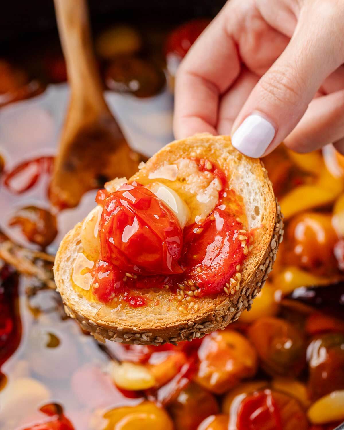 Hand holding piece of bread with tomato confit.