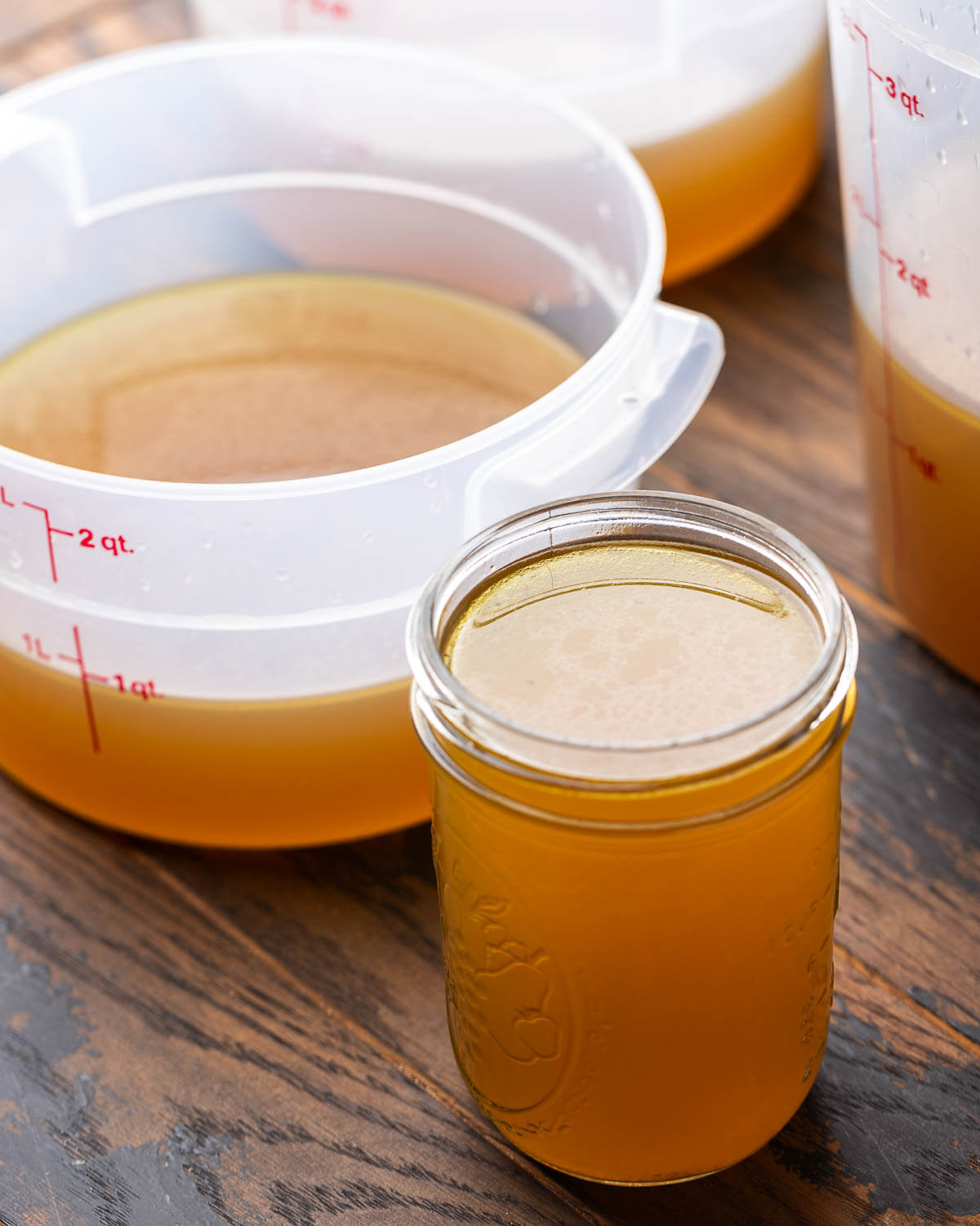 One mason jar filled with beef stock along with 3 Cambro containers partly filled.