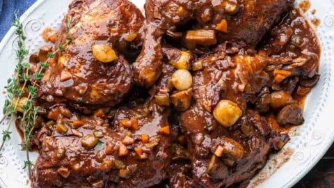 Coq au vin in white platter with thyme garnish.