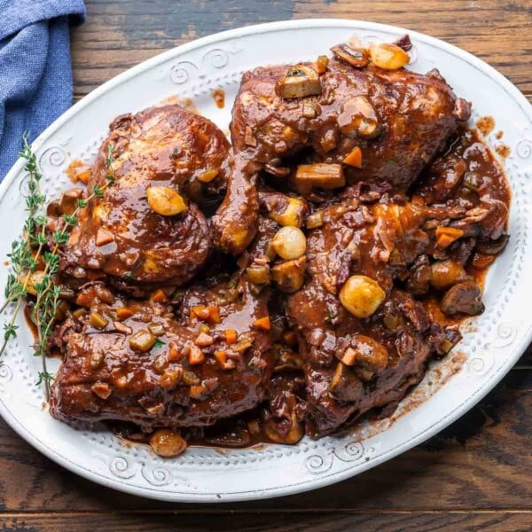 Coq au vin in white platter with thyme garnish.