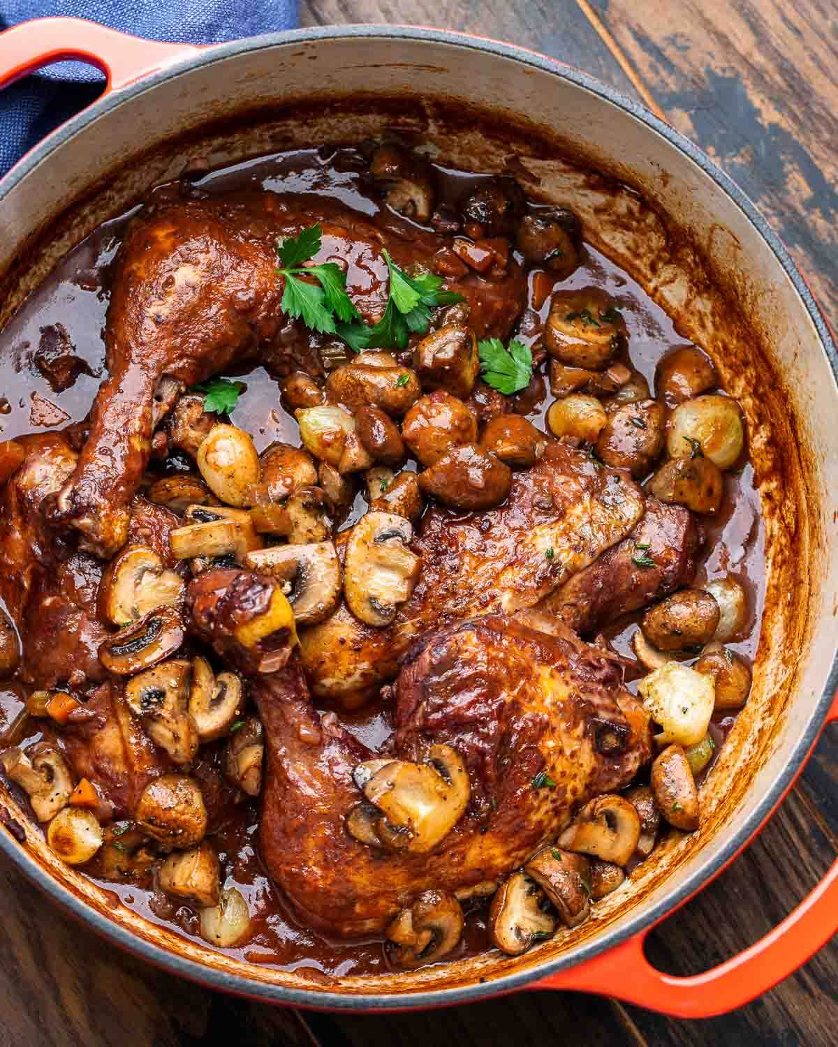 Overhead shot of coq au vin in Dutch oven on wood table.