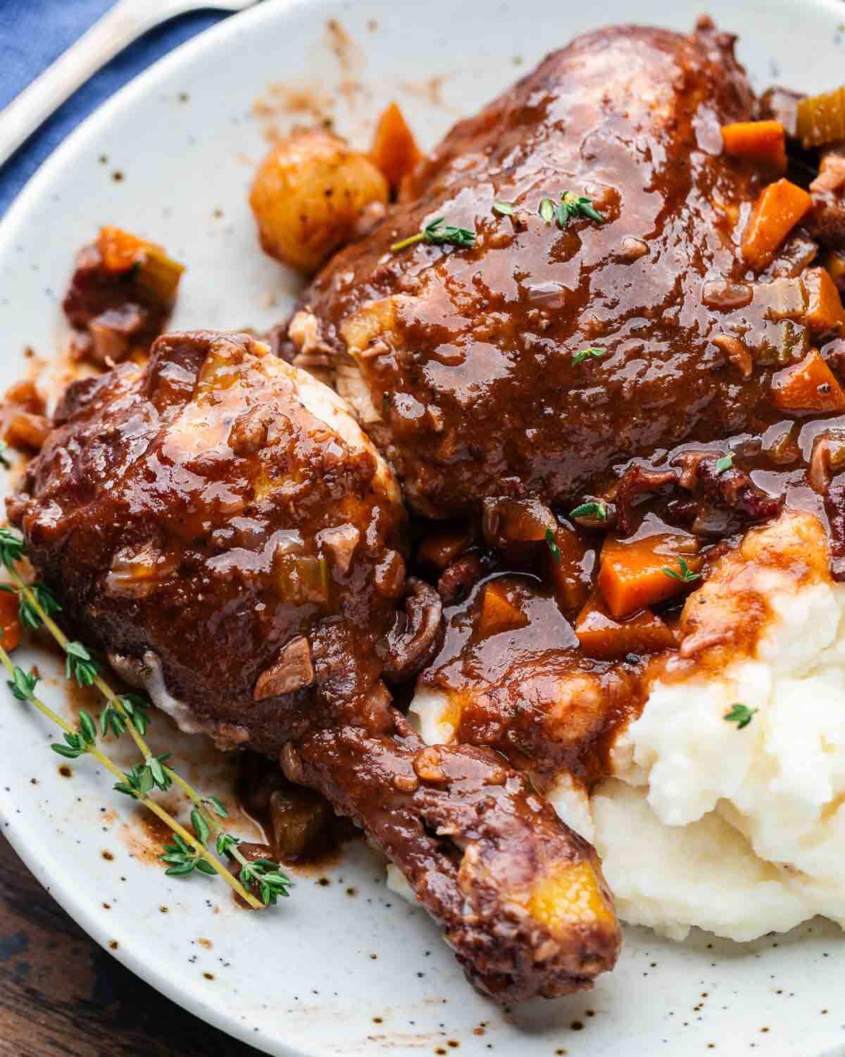 White plate with chicken thigh, leg, and mashed potatoes topped with wine sauce.