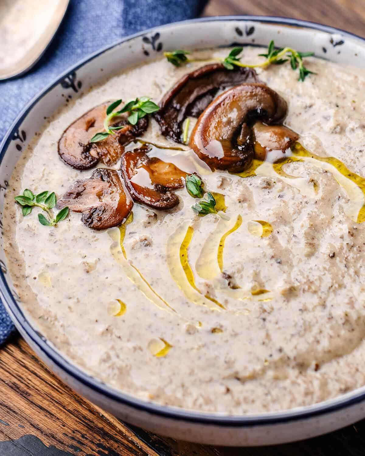 White and blue bowl with creamy mushroom soup along with mushroom and thyme garnish.