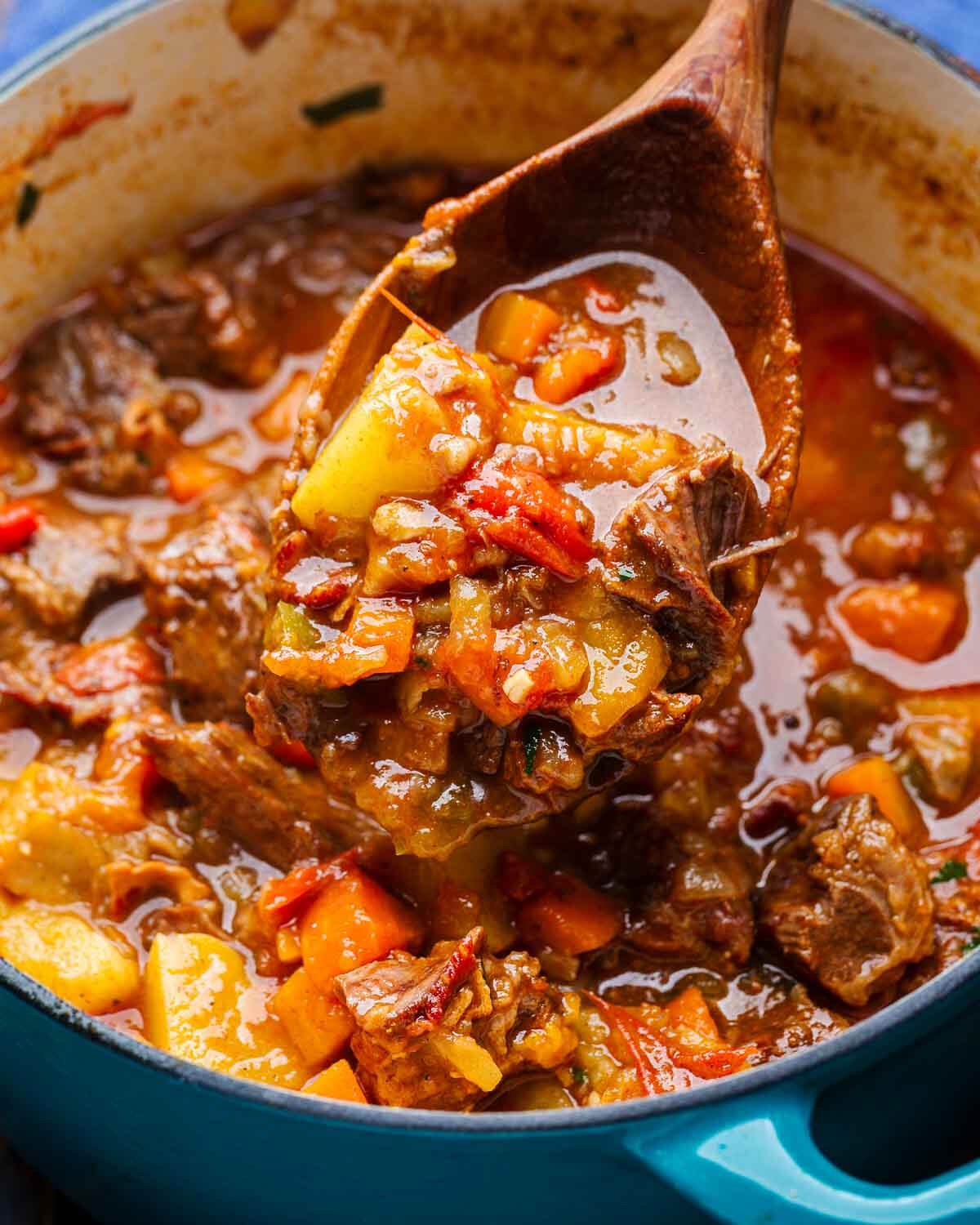 Large wooden ladle scooping out goulash over Dutch oven.