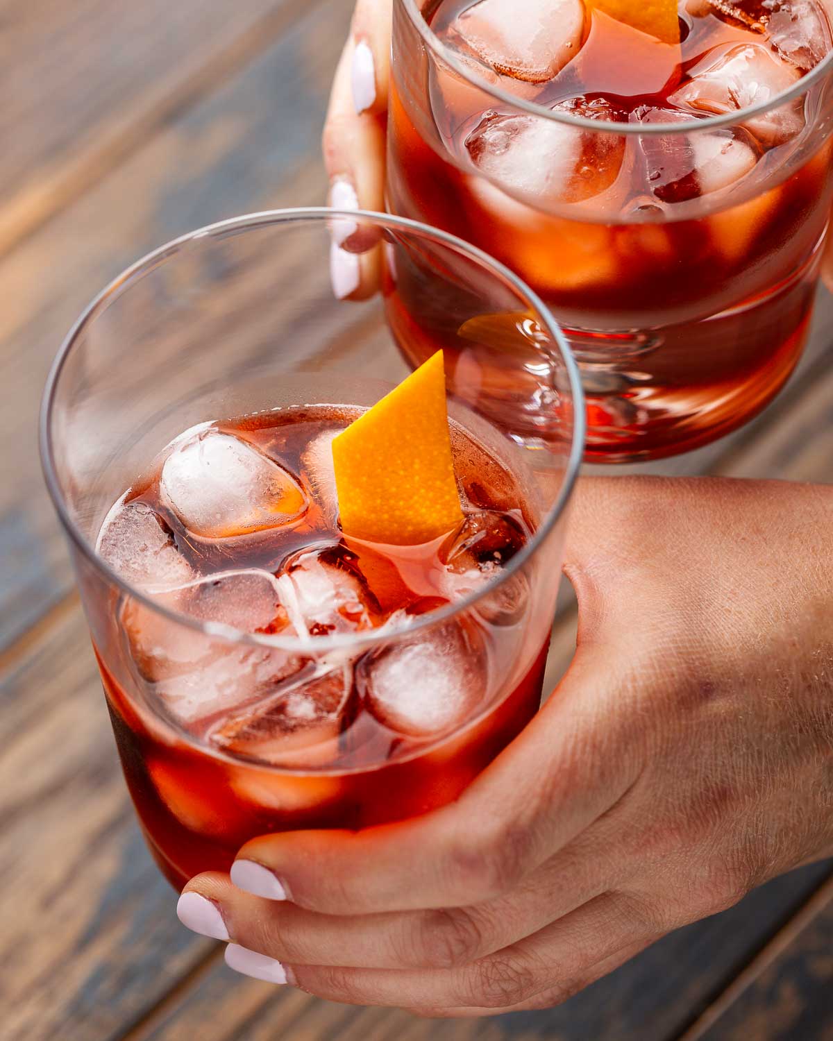 Hands holding two Negroni cocktails.