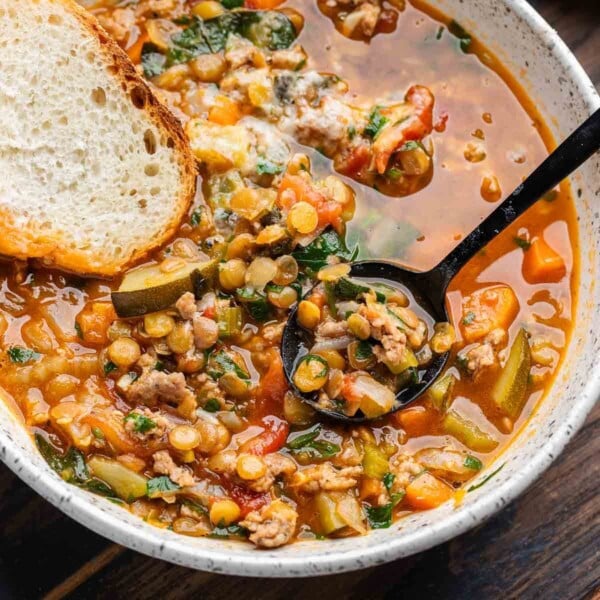Featured image showing sausage lentil soup in white bowl with slice of bread.