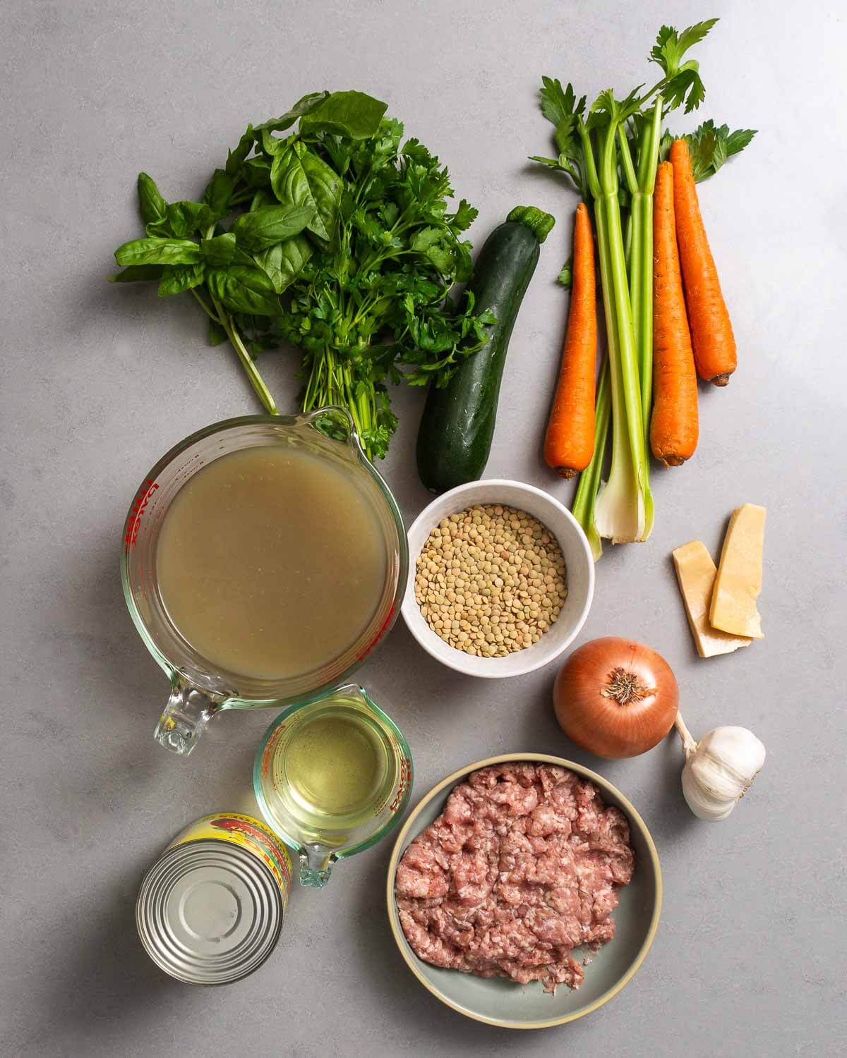 Ingredients shown: herbs, zucchini, carrots, celery, chicken stock, lentils, onion, parmesan rinds, sausage, tomatoes, garlic, and dry whtie wine.