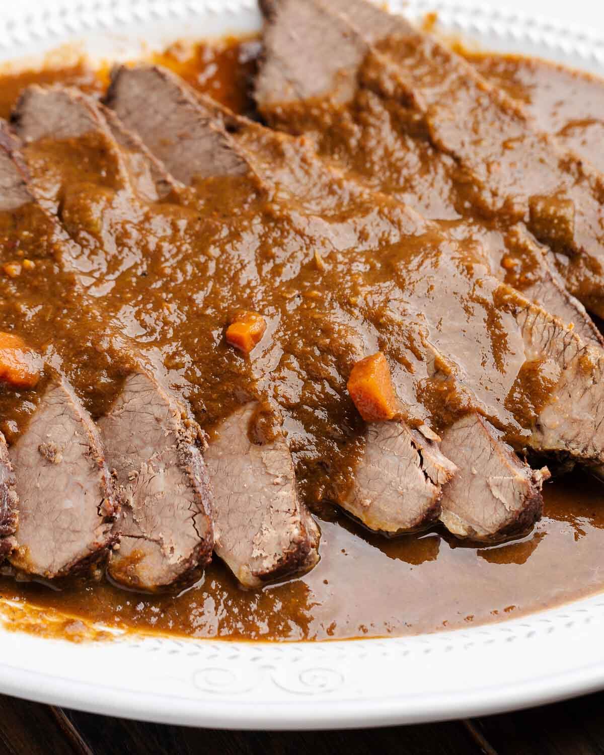 White platter with sliced brisket pieces with wine sauce.